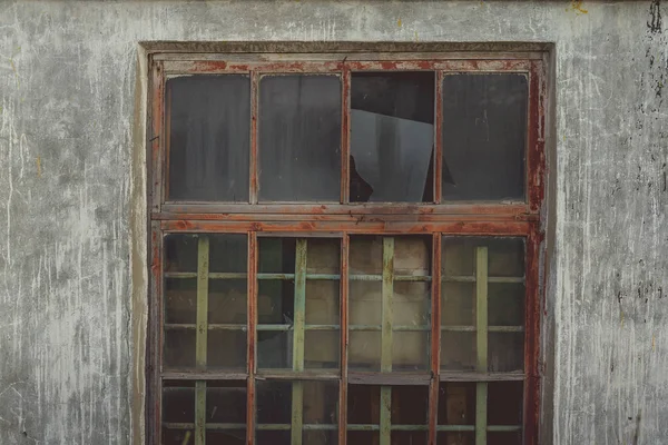 Eski ahşap pencere çerçevesinde kırık camlar ve eski terk edilmiş tuğla binada kısmen kırılmış camlar.