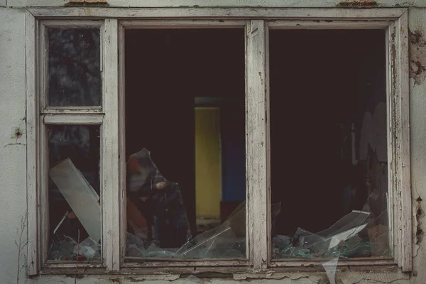 Eski ahşap pencere çerçevesinde kırık camlar ve eski terk edilmiş tuğla binada kısmen kırılmış camlar.