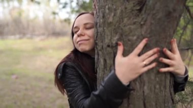 Gülümseyen güzel bir kadının portresi sonbahar ormanında duruyor ve ağacı kucaklıyor.