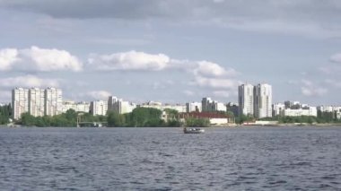 Nehir yeşil ağaçlarla çevrili olan mesafeye doğru ilerliyor. İnsanlar kayıkta kürek çekiyor.