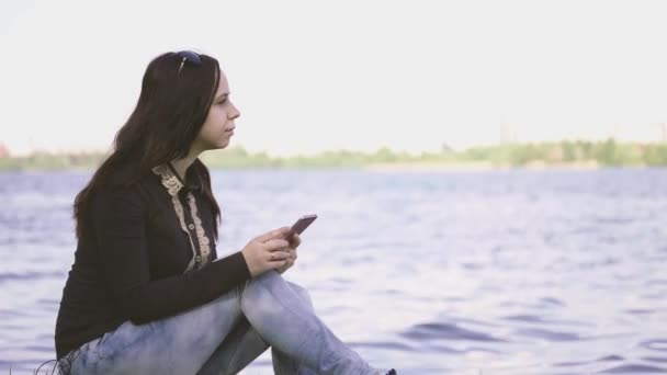 강둑에서 스마트폰을 사용하는 아름다운 — 비디오