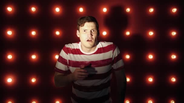 The man on the red background is shocked or horrified by what he saw , many light bulbs background above the red wall. shine. scene. Emotional man, the lights in the background — Stock Video