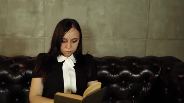 Mujer leyendo un libro en el sofá. Retrato de mujer de 20 años usando libro de lectura mientras descansa y se sienta en el sofá en el apartamento luminoso — Vídeos de Stock