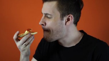 Pizza yiyen adam, turuncu arka planda yakın çekim. Erkek lezzetli bir yemek sahiptir