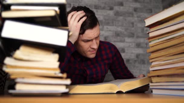 Man student tråkig läsbok på biblioteket med många böcker på universitetet. Student nedslagen läsbok för examination. — Stockvideo