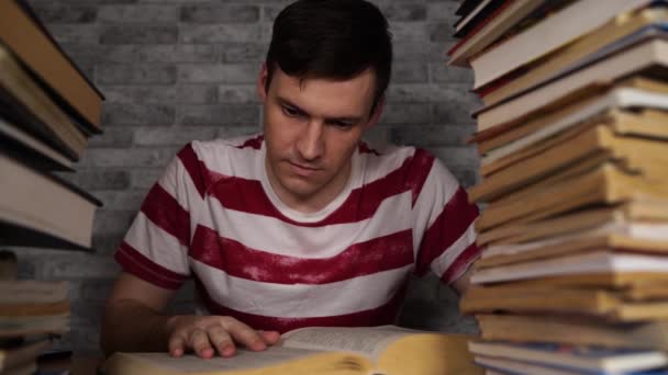 Hombre estudiante aburrido libro de lectura en la biblioteca con un montón de libros en la universidad. Estudiante descorazonado libro de lectura para el examen . — Vídeo de stock