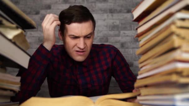 Man student tråkig läsbok på biblioteket med många böcker på universitetet. Student nedslagen läsbok för examination. — Stockvideo