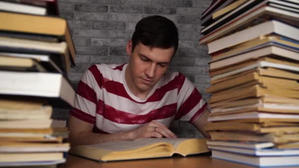 Üniversitede kitap bir sürü kütüphanede adam öğrenci sıkıcı okuma kitabı. Muayene için öğrenci disheartened okuma kitabı. — Stok video
