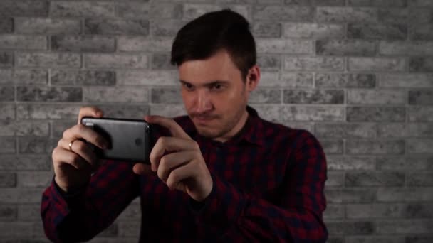 Un hombre toma fotos en un teléfono inteligente contra una pared de ladrillo — Vídeos de Stock