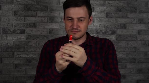 Ein Mann malt seine Lippen mit rotem Lippenstift gegen eine Ziegelwand — Stockvideo