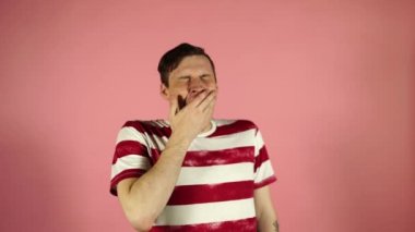 Bir t-shirt içinde genç bir adam, esniyor, pembe arka planda ayakta
