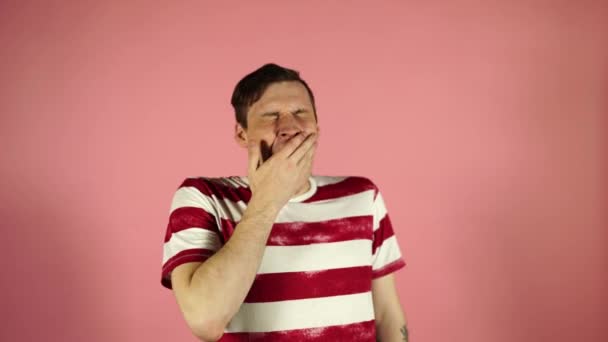 Een jonge man in een t-shirt, gaapt, staande op roze achtergrond — Stockvideo