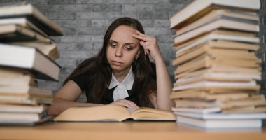 Üniversitede kitap bir sürü kütüphanede kadın öğrenci sıkıcı okuma kitabı. Muayene için öğrenci disheartened okuma kitabı.