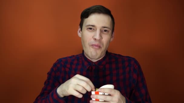 Un hombre comiendo papas fritas sobre un fondo naranja, primer plano . — Vídeos de Stock