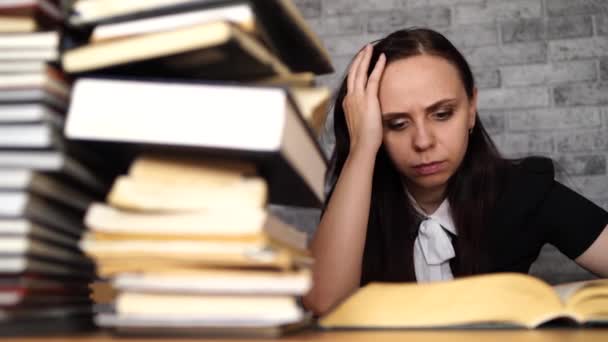 Estudiante aburrida leyendo libro en la biblioteca con un montón de libros en la universidad . — Vídeo de stock