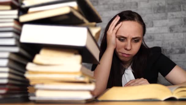 Estudiante aburrida leyendo libro en la biblioteca con un montón de libros en la universidad . — Vídeos de Stock