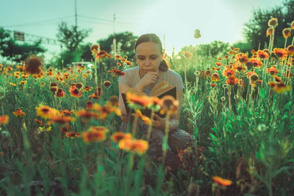 Žena čte knihu v zeleném poli, mezi trávou a květinami — Stock fotografie