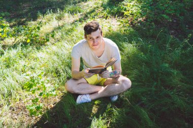 Genç yakışıklı adam açık alanda kitap okuyor.