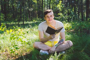 Yeşil bir yaz ormanında kitap okuyan adam.