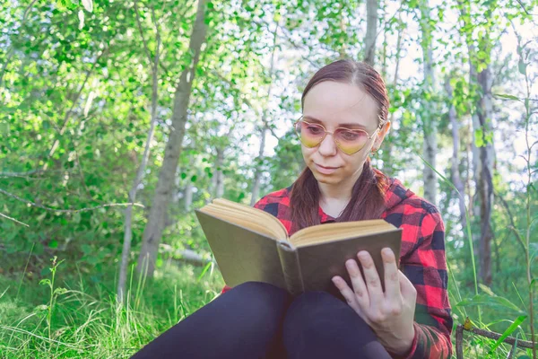 Een vrouw die een boek leest in een groen zomerwoud. — Stockfoto