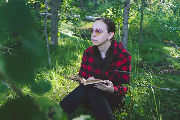 Egy nő könyvet olvas egy zöld nyári erdőben.. — Stock Fotó