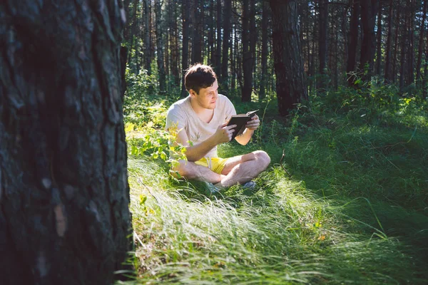 Man het lezen van een boek in een groene zomer bos. — Stockfoto