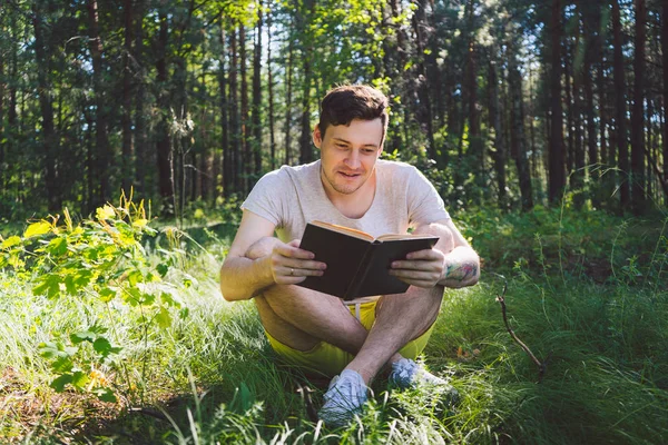 Ο άνθρωπος διαβάζει ένα βιβλίο σε ένα καταπράσινο καλοκαιρινό δάσος. — Φωτογραφία Αρχείου