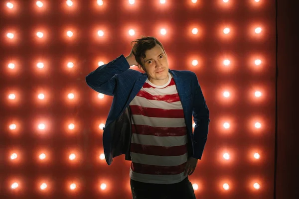 Junger Mann steht vor beleuchteter Wand. trendiger Mann blickt auf Kamera auf rotem Hintergrund mit Glühbirnen — Stockfoto