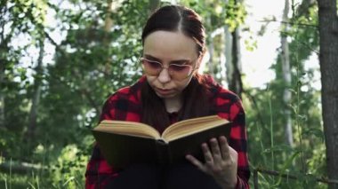 Yeşil bir yaz ormanında kitap okuyan bir kadın.