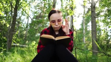 Yeşil bir yaz ormanında kitap okuyan bir kadın.