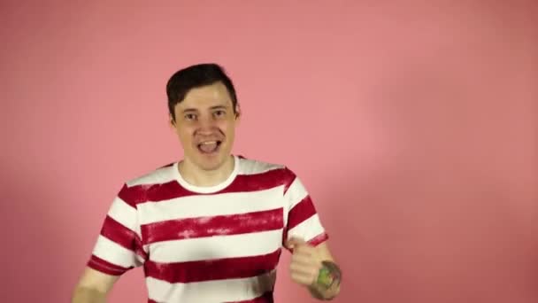 Счастливый мужчина с татуировкой танцует и смотрит на камеру на розовом фоне — стоковое видео