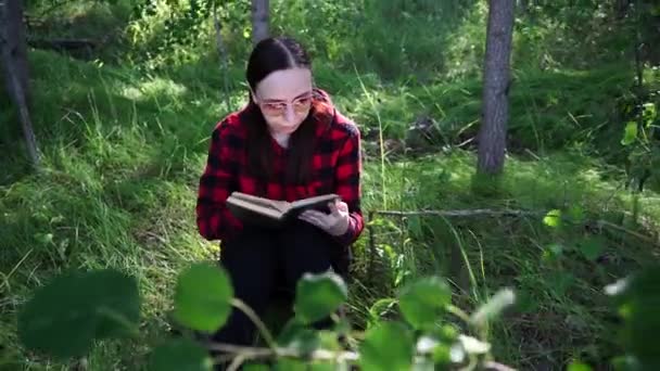 Een vrouw die een boek leest in een groen zomerwoud. — Stockvideo