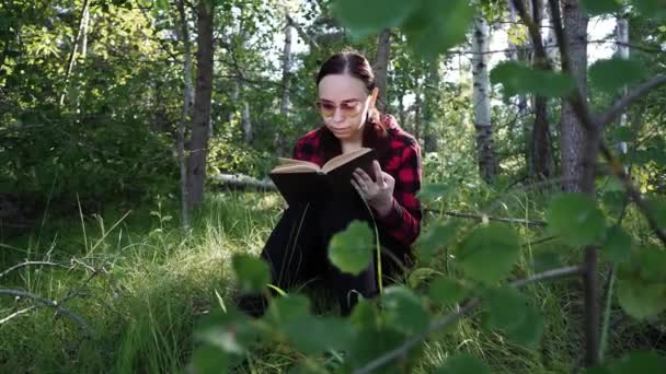 Egy nő könyvet olvas egy zöld nyári erdőben.. — Stock videók