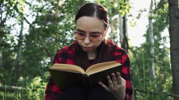 Kvinna läser en bok i en grön sommarskog. — Stockvideo