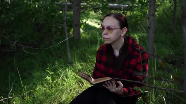 Жінка читає книгу в зеленому літньому лісі . — стокове відео