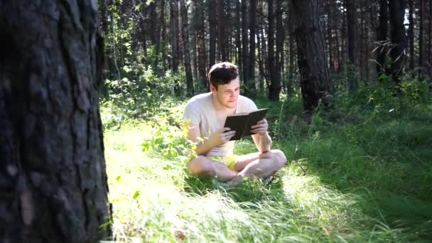 Man läser en bok i en grön Sommarskog. — Stockvideo