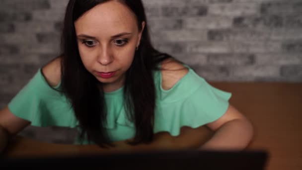 Jonge vrouw kijkt naar vertoning van laptop. Geconcentreerde brunette in blouse met naakte schouders browsen tijdens het werken op de computer tegen grijze muur — Stockvideo