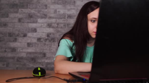 Jonge vrouw kijkt naar vertoning van laptop. Geconcentreerde brunette in blouse met naakte schouders browsen tijdens het werken op de computer tegen grijze muur — Stockvideo