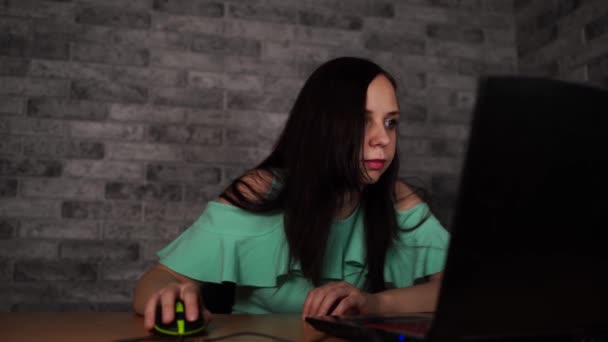 Jonge vrouw kijkt naar vertoning van laptop. Geconcentreerde brunette in blouse met naakte schouders browsen tijdens het werken op de computer tegen grijze muur — Stockvideo