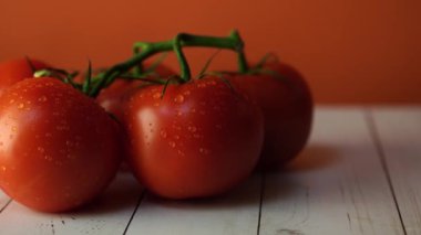 Masada su damlaları ile olgun domates. Yeşil sapları ve ahşap arka plan üzerinde su damlaları ile iştah açıcı olgun kırmızı domates