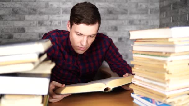 Студент-чоловік нудний читає книгу в бібліотеці з великою кількістю книг в університеті. Студент розчарований читанням книги для іспиту . — стокове відео