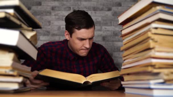 Hombre estudiante aburrido libro de lectura en la biblioteca con un montón de libros en la universidad. Estudiante descorazonado libro de lectura para el examen . — Vídeos de Stock