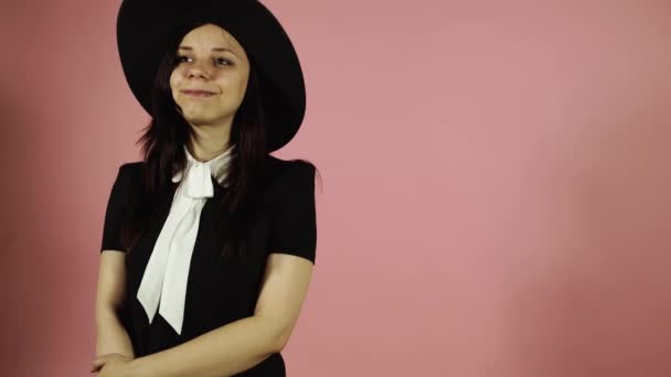 Senhora sorrindo em um fundo rosa. Uma mulher com um vestido preto e um chapéu . — Vídeo de Stock
