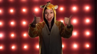Kadın kırmızı bir arka plan üzerinde başparmak ile gibi yapıyor. Parlak çocuklu bir kadın kanguru şeklinde pijama. çocuk animatör kostüm sunumu.