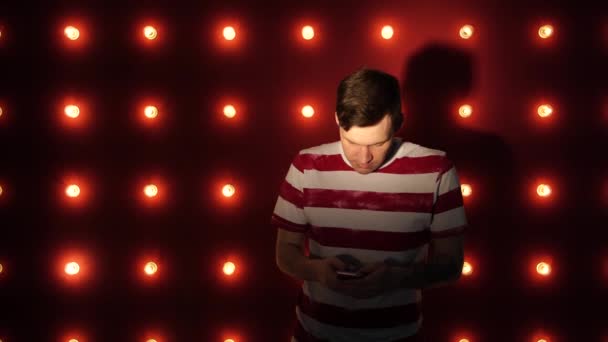 Jovem feliz em pé por uma parede iluminada usando smartphone. Conceito: feliz ou boa notícia — Vídeo de Stock