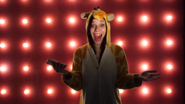 Gelukkige jonge vrouw staande door een verlichte muur met behulp van smartphone. Concept: gelukkig of goed nieuws. Vrouw in een lichte Childrens pyjama in de vorm van een kangoeroe. — Stockvideo