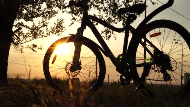 Hermosa escena de cerca de la bicicleta al atardecer, sol en el cielo azul con colores vintage, silueta de la bicicleta hacia adelante al sol . — Vídeo de stock
