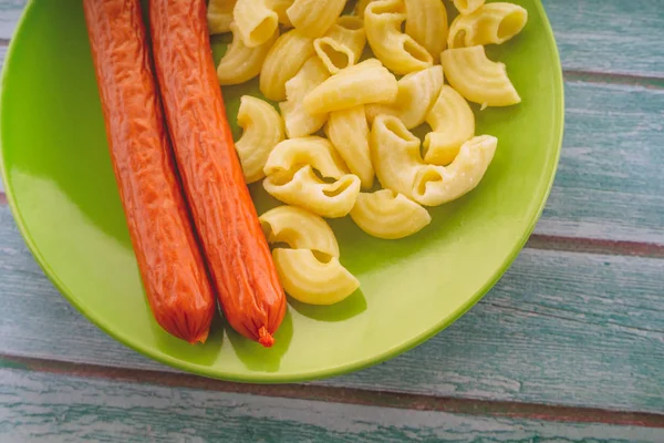 Pasta e salsicce in un piatto verde su un tavolo di legno. pasta in primo piano — Foto Stock