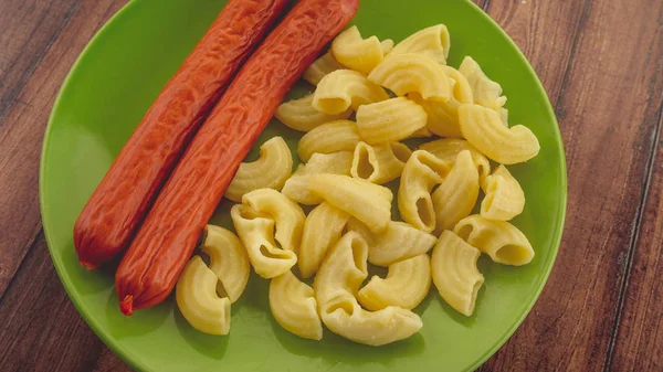 Pasta and sausages in a green plate on a wooden table. pasta in closeup — Stock Photo, Image