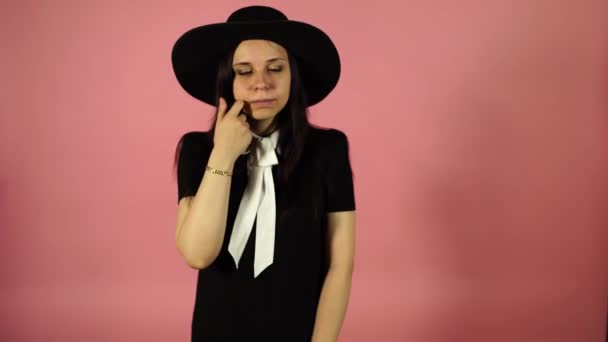 Señora sonriendo sobre un fondo rosa. Una mujer con un vestido negro y un sombrero . — Vídeo de stock